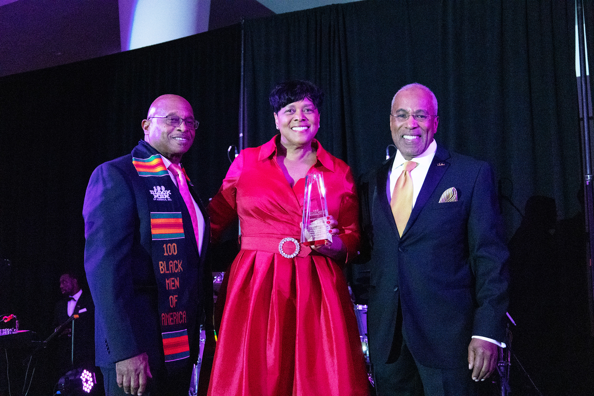 Three people on stage holding an award, smiling and celebrating their achievement together